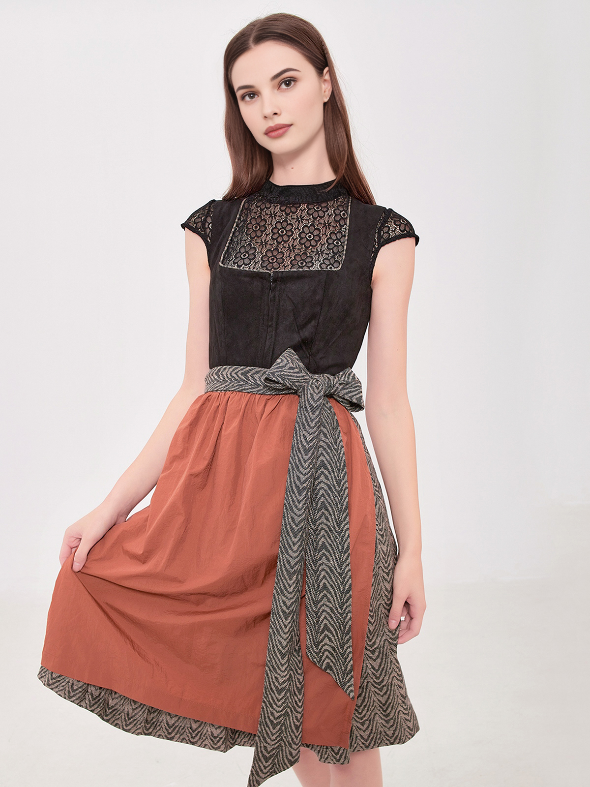 Ein elegantes schwarzes Dirndl mit weißer Bluse und roter Schürze